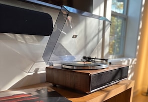 A turntable on a wooden table near a window with a view of trees.