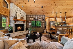 A cozy living room with a stone fireplace, wooden ceiling, and a television mounted on the wall.