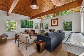 Ein großzügiges Wohnzimmer mit einem blauen Sofa, Holzboden und großen Fenstern mit Blick ins Freie.