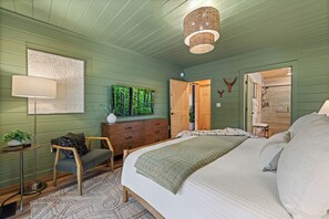 A bedroom with a bed, dresser, chair, lamp, and artwork.