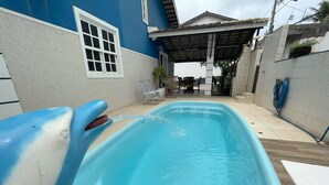 Une piscine avec un toboggan, entourée d’un patio couvert comprenant des chaises et une table.