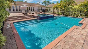 Relax by the pool surrounded by lush greenery and a brick deck.