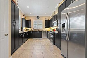 Fully equipped kitchen with refrigerator, microwave, and oven, plus a window and clock.