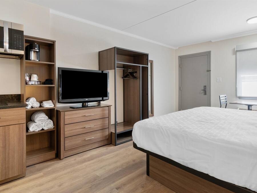 A modern hotel room with a flat-screen TV, wooden furniture, a wardrobe, and a bed.