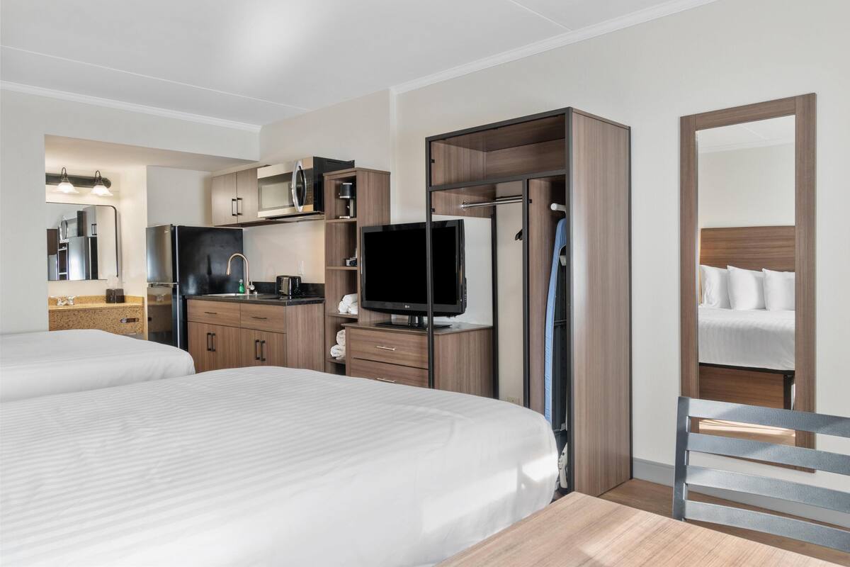 Ein Hotelzimmer mit zwei Betten, einer Küchenzeile, einem Fernseher und einem Spiegel.