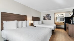 Hotelkamer met twee bedden, een kitchenette en een badkamer met spiegel en wastafel.