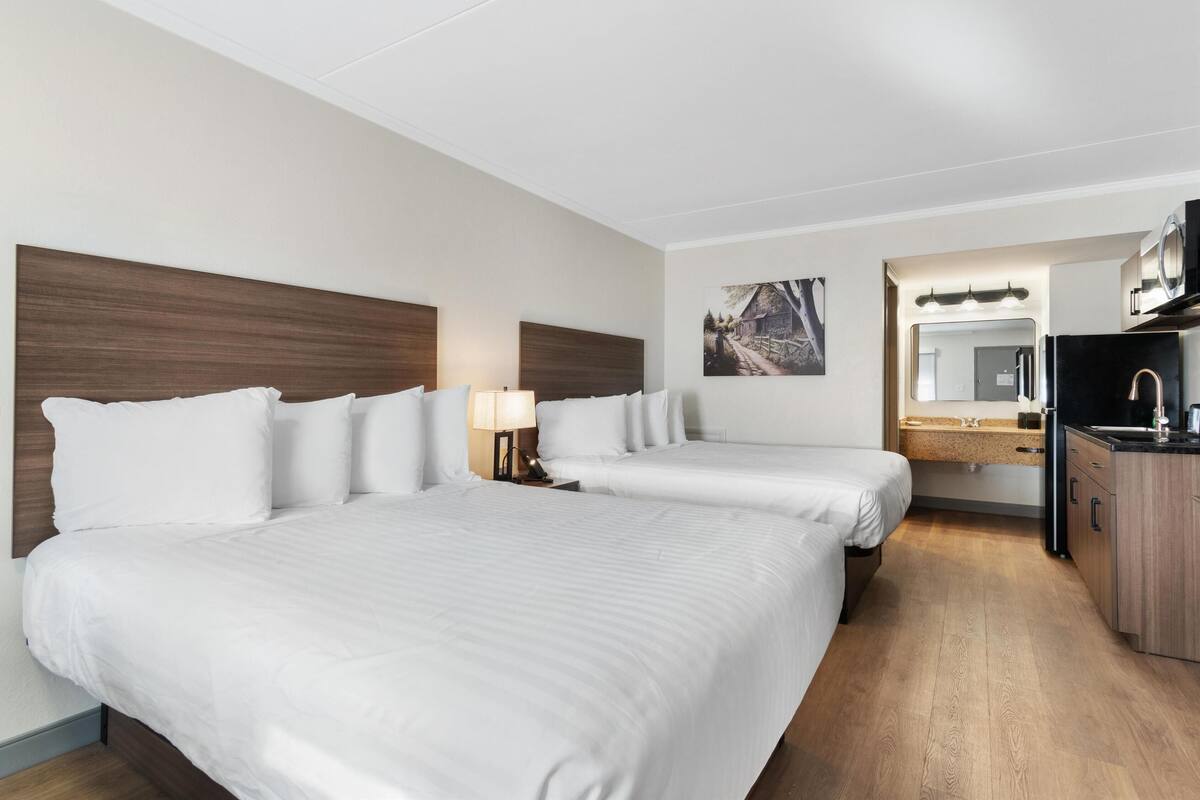Ein Hotelzimmer mit zwei Betten, einer Küchenzeile und einem Badezimmer mit Spiegel und Waschbecken.