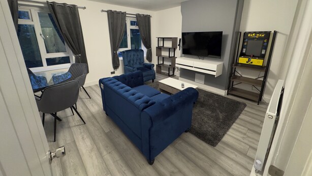 Ein modernes Wohnzimmer mit einem blauen Sofa, einem Fernseher und einer Pac-Man Arcade-Maschine.