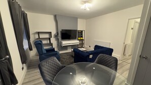 Ein modernes Wohnzimmer mit einem Glastisch, zwei blauen Sofas, einem Fernseher und einem kleinen weißen Schrank.