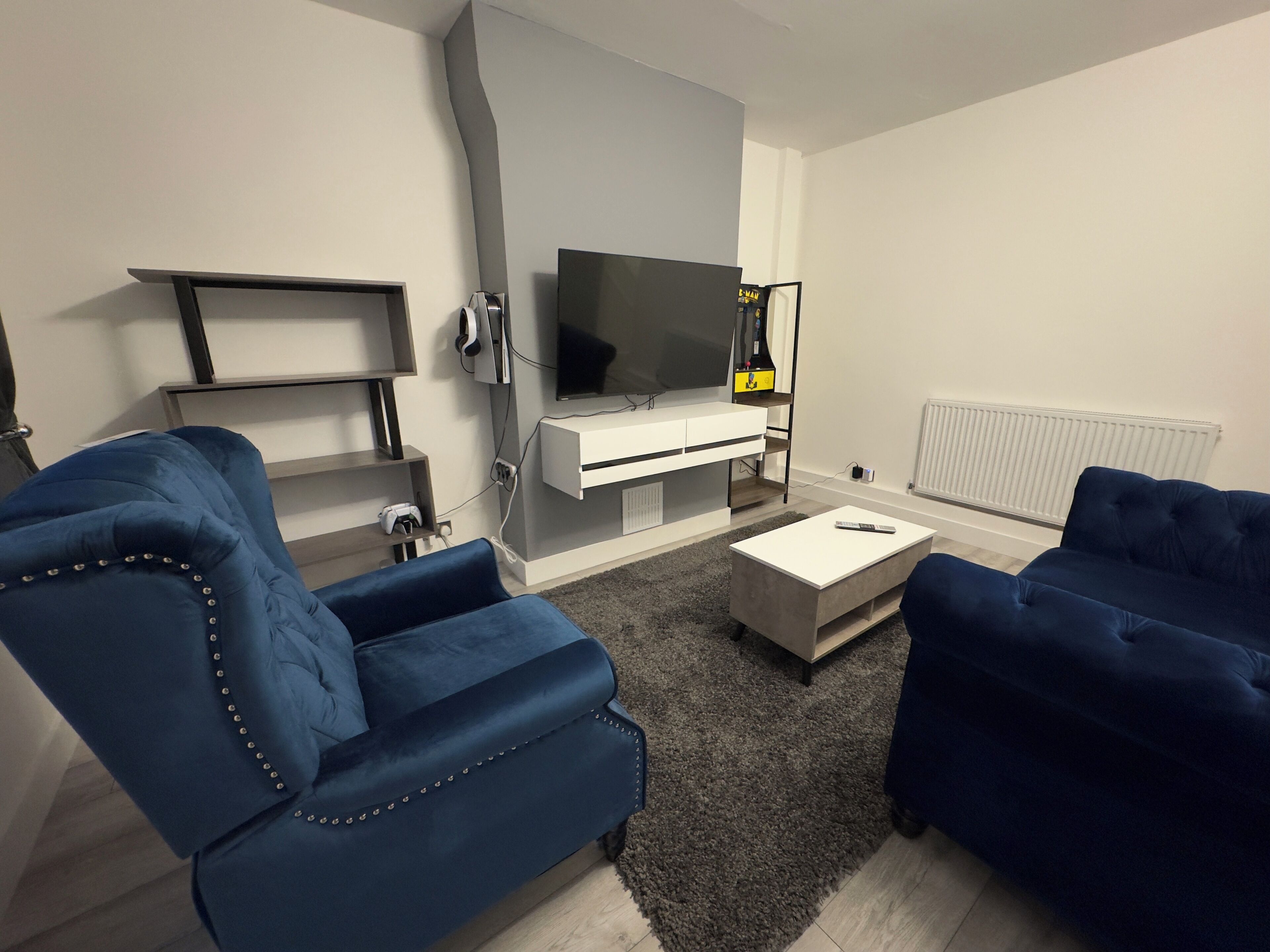 Een moderne woonkamer met een flatscreen televisie, twee blauwe banken, een witte salontafel en een grijze accentmuur.
