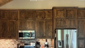 A kitchen with wooden cabinets, a stainless steel refrigerator, a microwave, an oven, and a coffee maker. - Cosy 1-bedroom cottage with spring-fed creek and spectacular views (Kerrville)