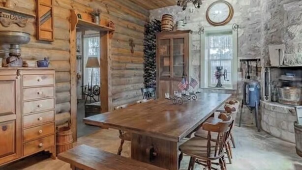 A rustic wooden interior with a long dining table, wooden cabinets, and a stone wall.