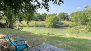 A picnic table and a blue chair in a park with a pond and trees in the background.