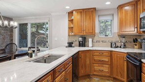 A modern kitchen with wooden cabinets, a large island with a sink, and a stone backsplash. - Lodge Tower 199 2BR  at the base of Vail Mountain (Vail)