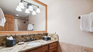 A bathroom with a granite countertop, wooden cabinets, a large mirror, and a towel rack.