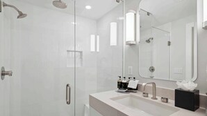 A modern bathroom with a glass-enclosed shower, a large mirror, and a vanity with a sink and countertop.