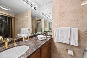 Une salle de bain moderne avec un grand lavabo, des robinets dorés, des plans de travail en marbre et un grand miroir.
