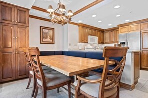 Une cuisine avec des meubles en bois, une table à manger avec des chaises, un lustre et un four à micro-ondes.