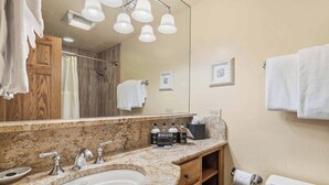 A bathroom with a granite countertop, a sink, a mirror, and a toilet. There are towels hanging on the wall and a shower curtain.
