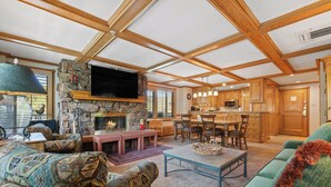 A spacious living room with a stone fireplace, wooden ceiling beams, a television, and a dining area with wooden cabinets. - Lodge Tower 599 1BR  at the base of Vail Mountain (Vail)