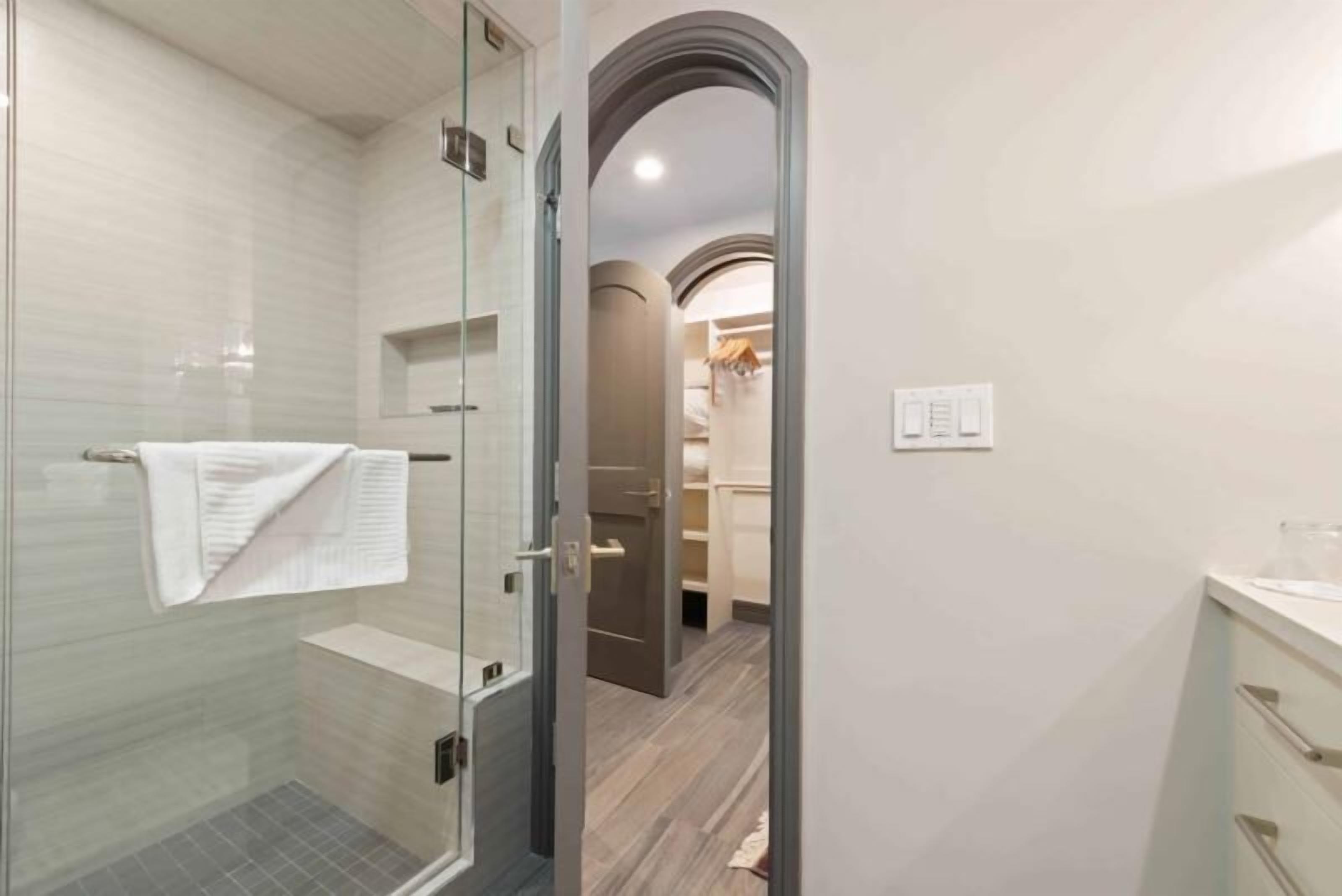 A modern bathroom with a glass shower enclosure, a white towel hanging on the wall, and a wooden floor.