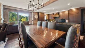 Une cuisine moderne avec des meubles en bois, une grande table à manger entourée de chaises et des luminaires suspendus.