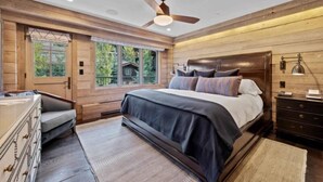 Une chambre avec un grand lit, des murs en bois, un ventilateur de plafond et une vue sur la verdure environnante.