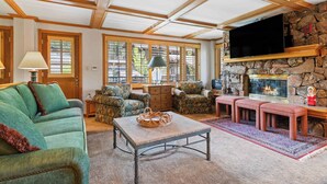 A cozy living room with a stone fireplace, comfortable seating, and large windows.