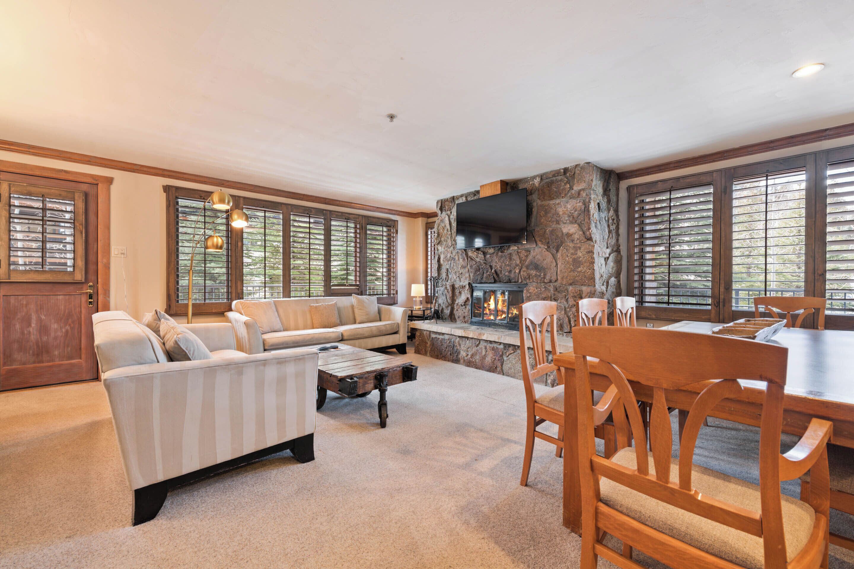 A spacious living room with a stone fireplace, a large sofa, a dining table, and wooden chairs.