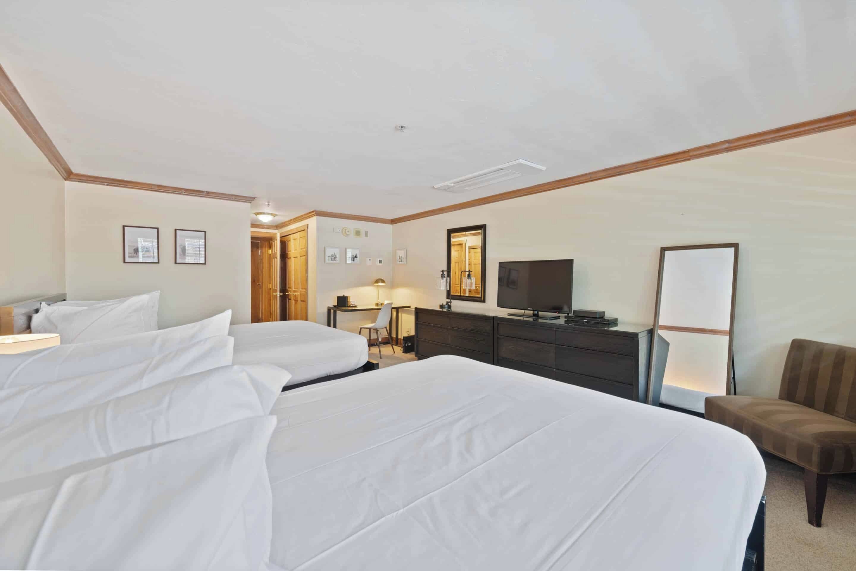 A hotel room with two beds, a desk, a chair, a TV, and a mirror.