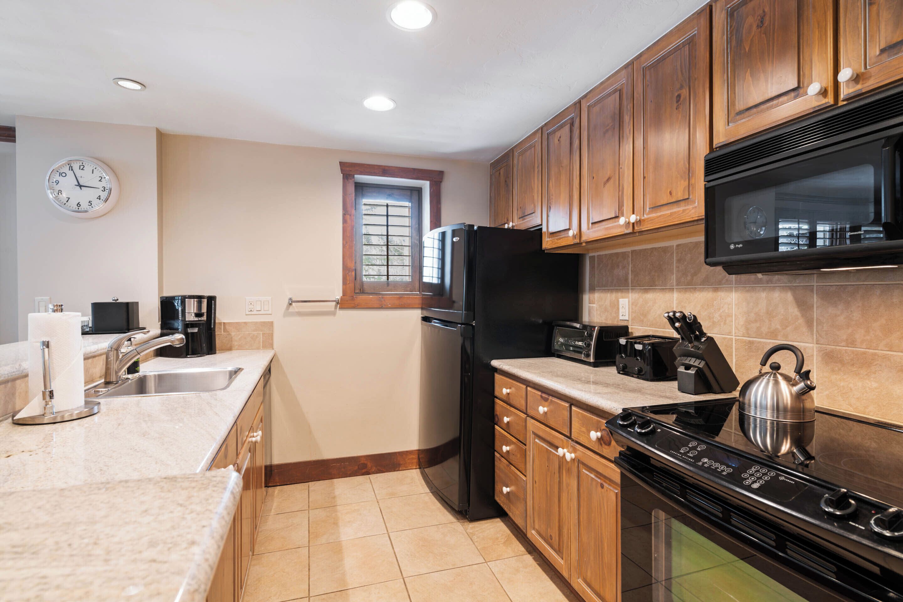 A kitchen with wooden cabinets, a stainless steel refrigerator, a microwave, a stove, and a window with blinds.
