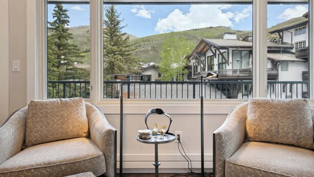 A room with two armchairs, a small table with decorative items, and a view of a mountain landscape through large windows. - Lodge Tower 278 1BR at the base of Vail Mountain (Vail)
