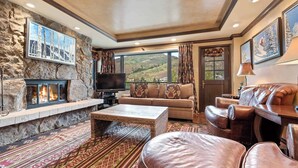 A cozy living room with a stone fireplace, a large flat-screen TV, a sofa, and leather armchairs.