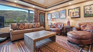 A living room with a sofa, leather chairs, a coffee table, and a large window with a view of a hilly landscape.