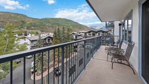 A balcony with a view of a residential area, a parking lot, and mountains in the distance.
