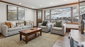 A living room with a sofa, armchairs, a coffee table, and a fireplace. Large windows offer a view of a snowy landscape. - Lodge Tower 678 1BR at the base of Vail Mountain (Vail)