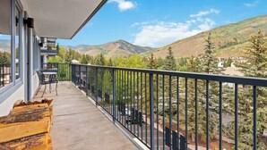 A balcony with a view of mountains, a table with chairs, and wooden benches.