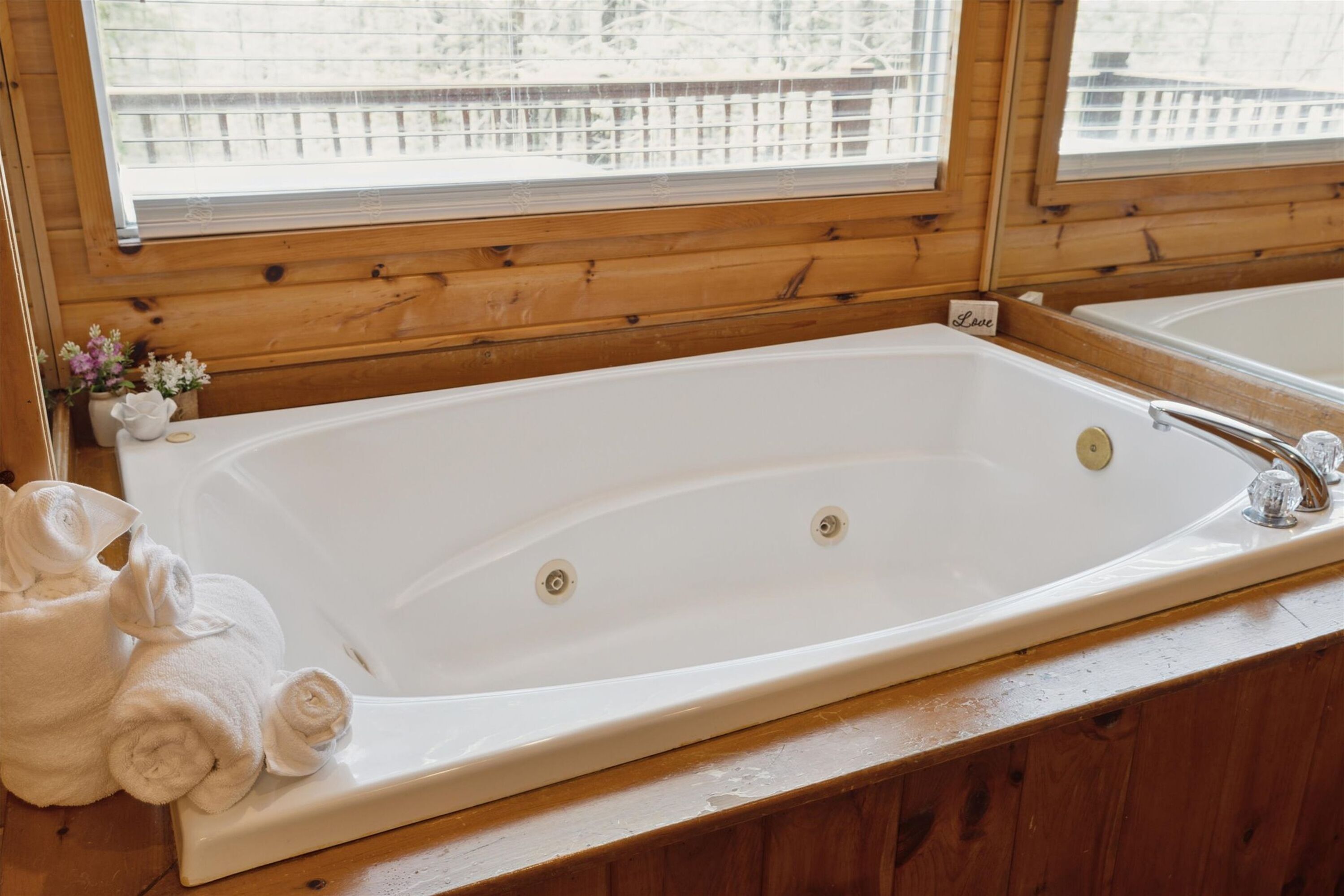 A large white bathtub with a faucet, a small sign reading "Love", and towels placed beside it.