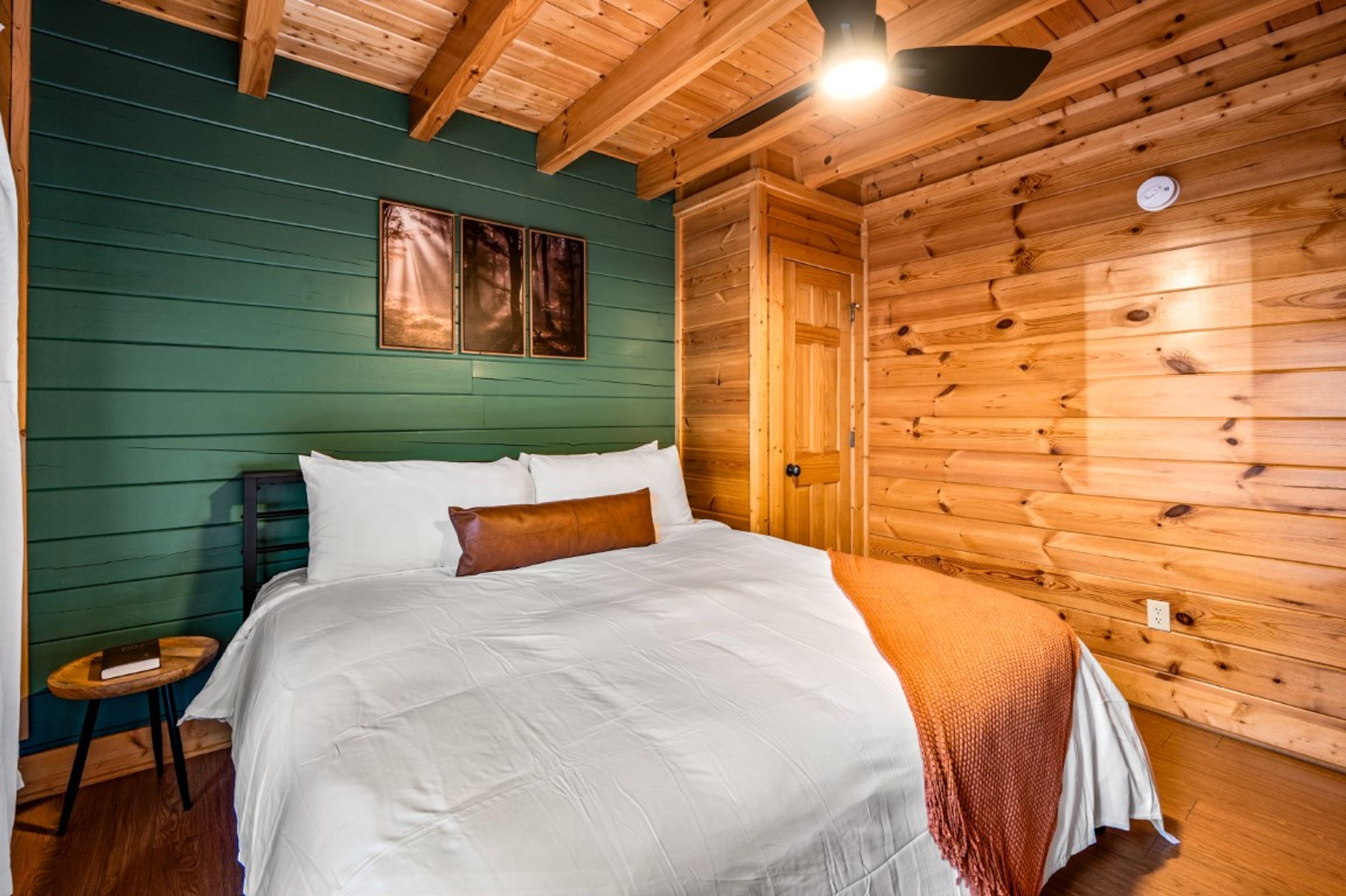 Ein Zimmer einer Holzhütte mit einem Bett, einem Deckenventilator und einer Tür.