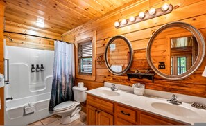 A wooden cabin bathroom with a bathtub, toilet, and double sink vanity. - Amazing Views w Gameroom Hot Tub Pool (Sevierville)
