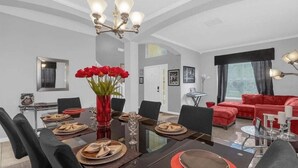 Ein moderner Essbereich mit einer Deckenleuchte, einer roten Vase mit Blumen und einem roten Sofa im Wohnbereich.