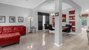 Ein modernes Wohnzimmer mit einem roten Sofa, einem Essbereich mit schwarzen Stühlen und einer Küche mit roten Akzenten.