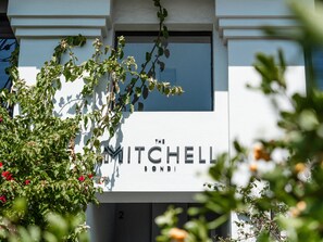 The Mitchell Bondi features a sleek, modern facade amidst lush surroundings.