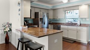 Une cuisine moderne dotée d’un îlot central, de meubles blancs, d’appareils électroménagers en acier inoxydable et d’un ventilateur de plafond.