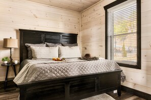 A wooden-paneled bedroom with a bed, a nightstand, a lamp, and a window with blinds. - Million $ View|Indr Pool|Games|Pool Table|Theater (Sevierville)