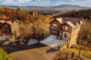 A large, two-story log cabin with a stone foundation and a steeply pitched roof, surrounded by a well-maintained yard and a scenic mountain backdrop. - Million $ View|Indr Pool|Games|Pool Table|Theater (Sevierville)