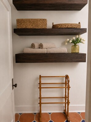 Une pièce avec trois étagères en bois, un panier en osier, des serviettes enroulées, un vase avec des fleurs et un étendoir en bois.