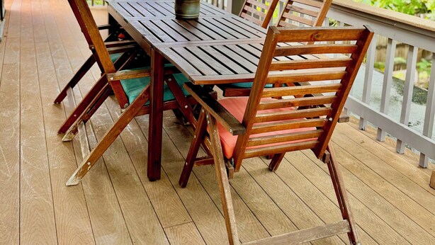 Eine Holzterrasse mit Tisch und Stühlen, umgeben von Bäumen.