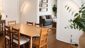 Ein Essbereich mit Holztisch und -stühlen, einer Couch und einem an der Wand befestigten Regal.