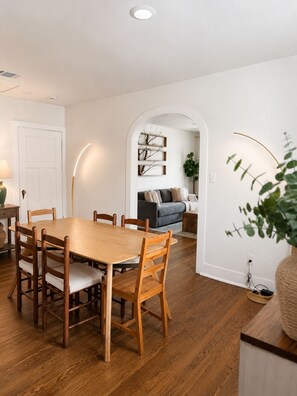 Un coin repas avec une table et des chaises en bois, un canapé et une étagère fixée au mur.
